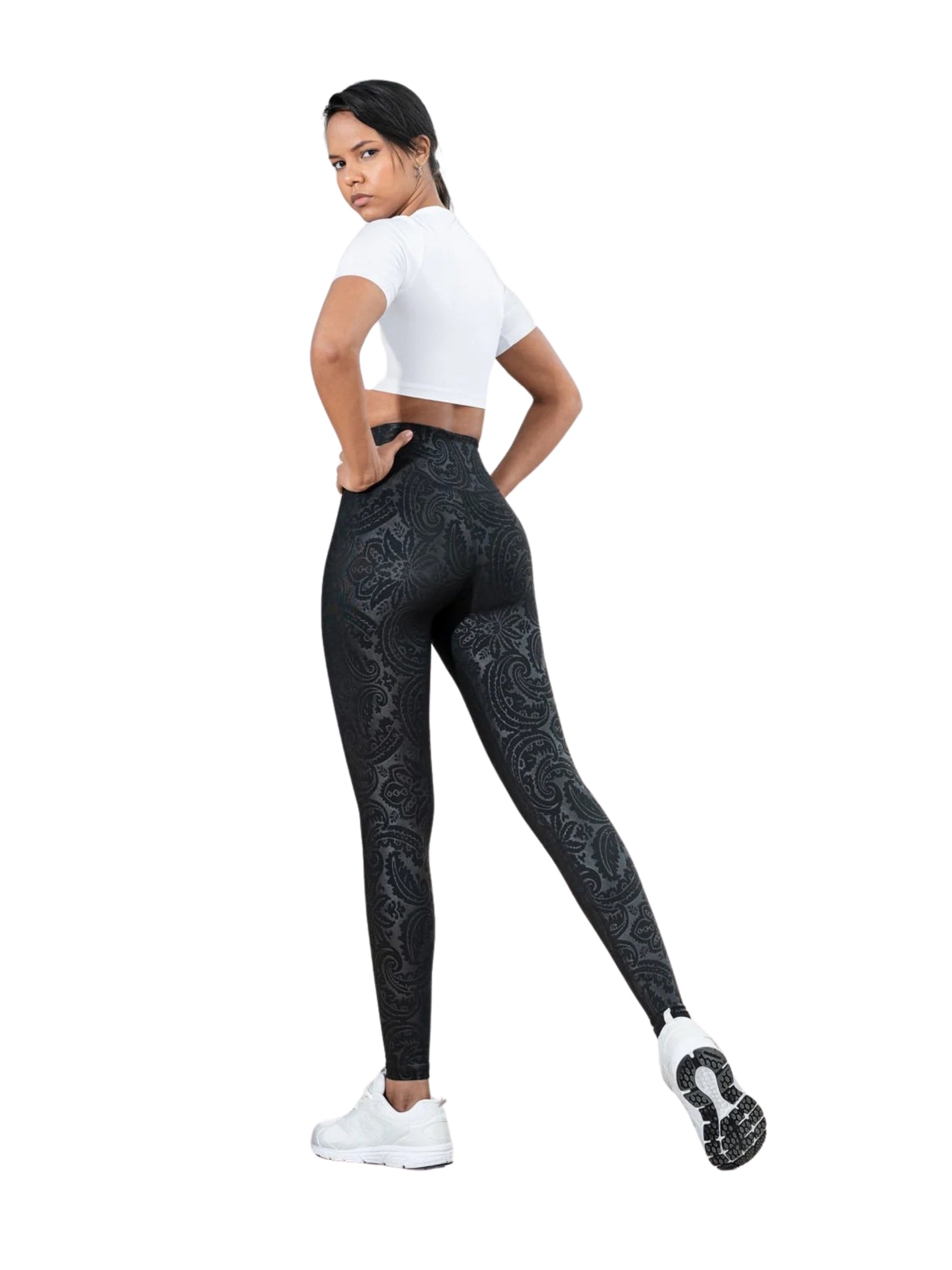 Person in einem weißen Oberteil, die Lisminas Bilboa-Leggings in Lederoptik in Schwarz trägt und mit einem angewinkelten Bein posiert.